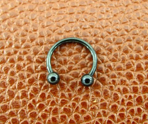 cherna-titanieva-obeca-podkova-za-piersing Черна титаниева обеца подкова за ухо и устна върху кафява кожена повърхност