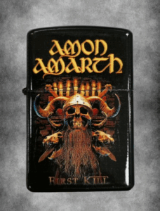 Черна бензинова запалка на Amon Amarth First Kill Заглавие на снимка: cherna-benzinova-zapalka-amon-amarth-first-kill Описание на снимка: Черна метална бензинова запалка с детайлен цветен принт на викингски череп с рога и златисто лого на групата Amon Amarth First Kill.
